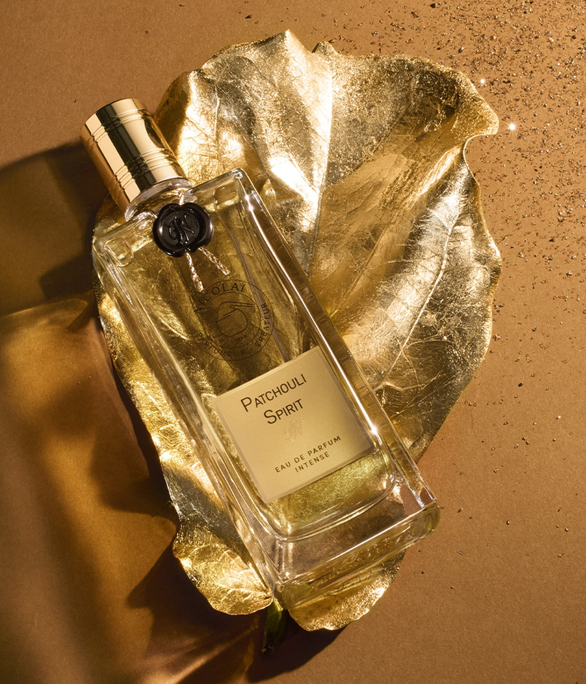 Nicolaï Eau de Parfum Patchouli Spirit liegend auf einem goldenen Blatt vor ockerfarbenem Grund