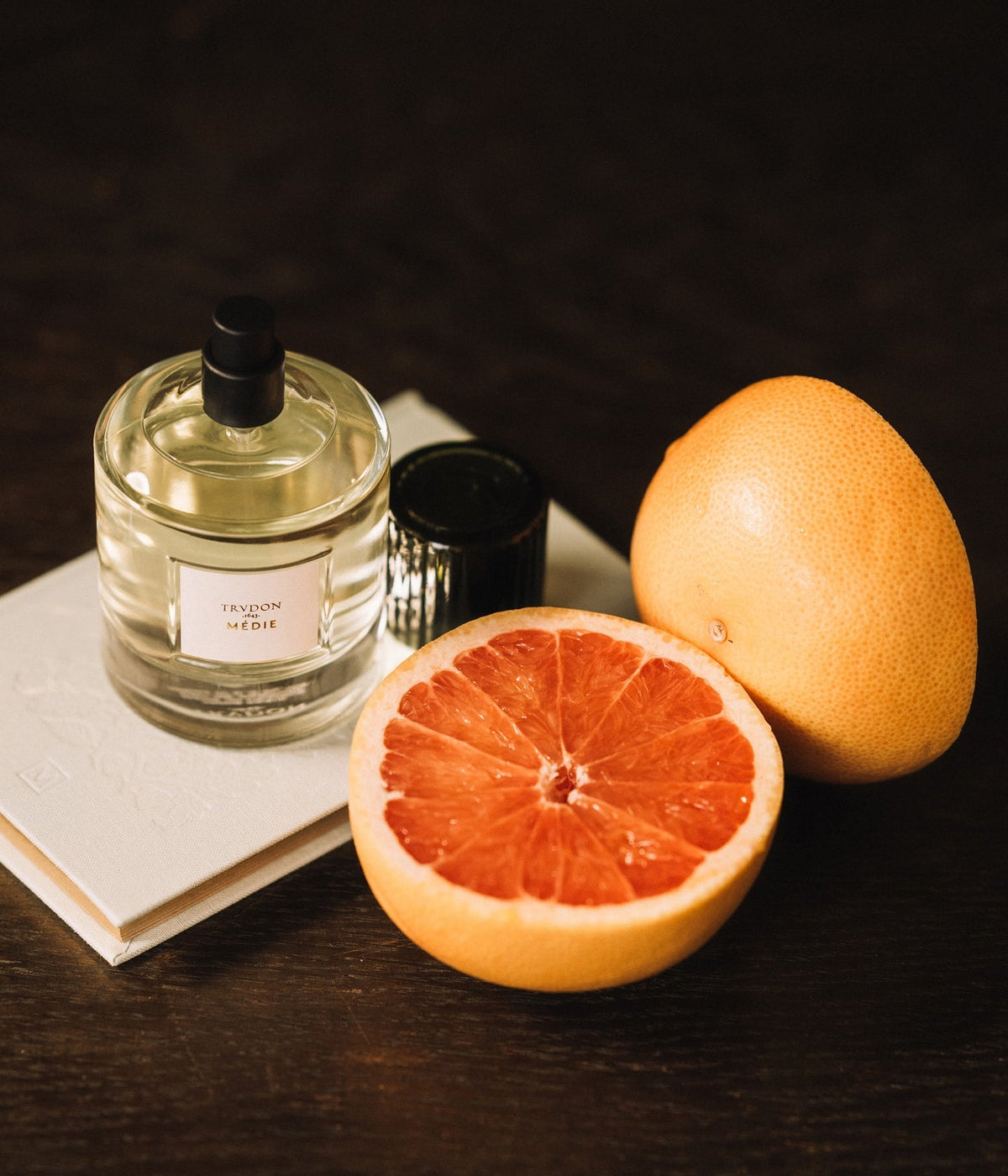 Trudon Eau de Parfum Médie next to a halved grapefruit on a book