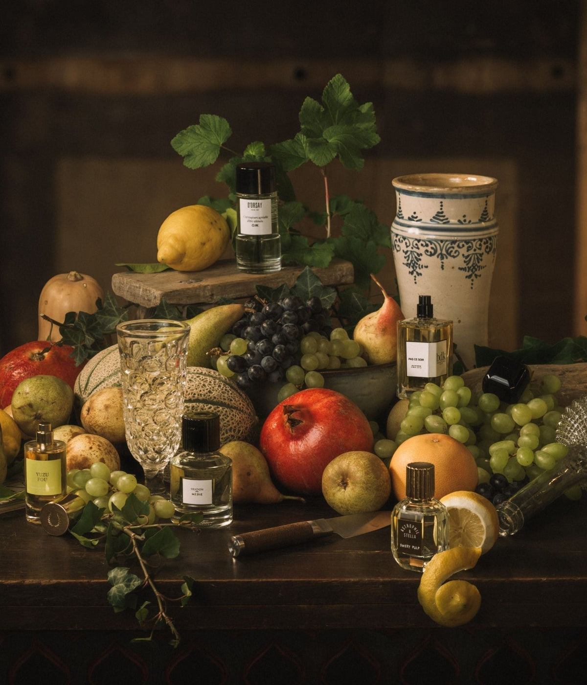 Duft und Kultur Editorial – Früchte der Versuchung, Stillleben mit Parfumflakons zwischen Granatäpfeln, Trauben, Birnen und Zitronen