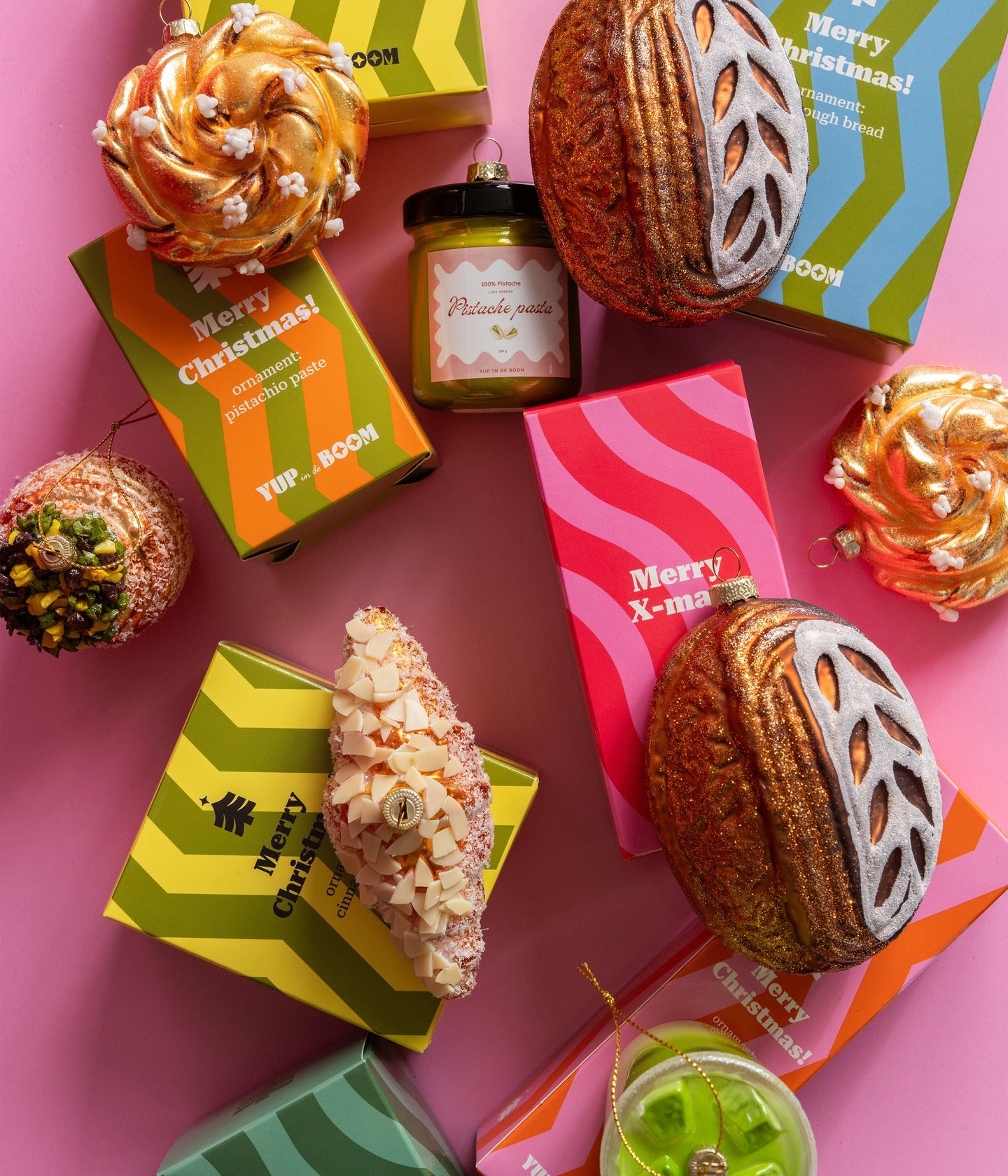 Yup in de boom Christbaumschmuck, Zimtschnecken, Sauerteigbrote, Pistaziencreme und Mandelcroissant mit Verpackungen auf rosa Grund