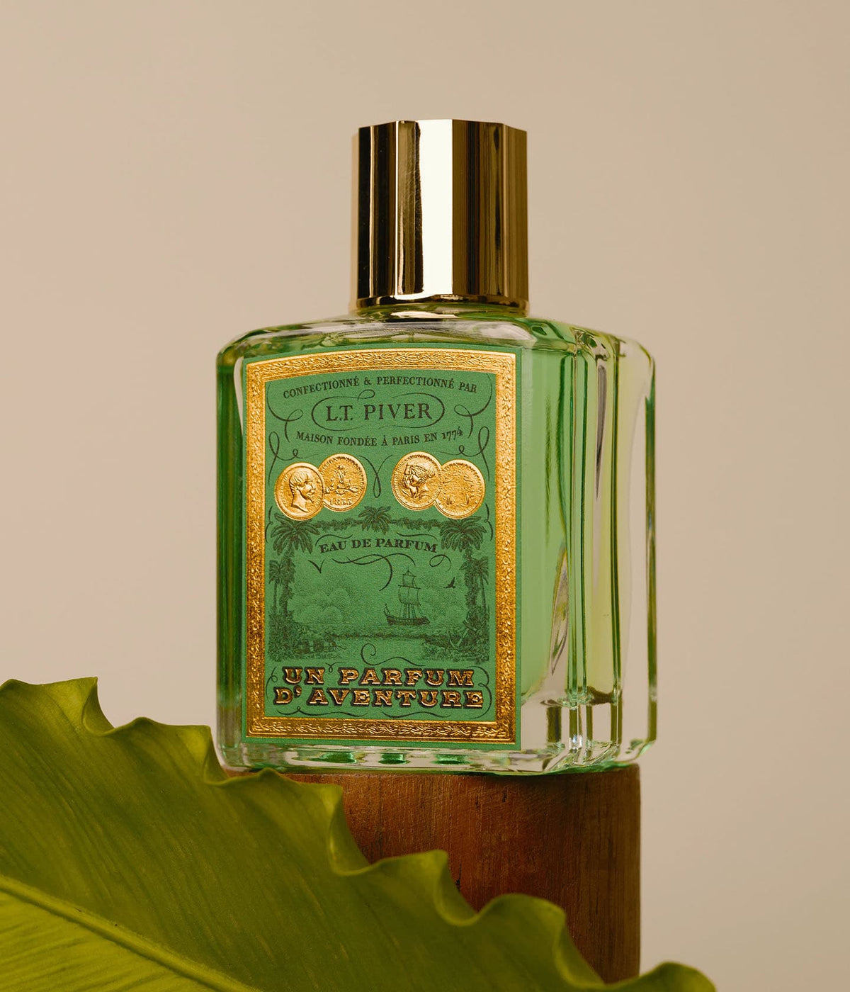 L.T. Piver Eau de Parfum Un Parfum d’Aventure on a wooden pedestal with a palm leaf