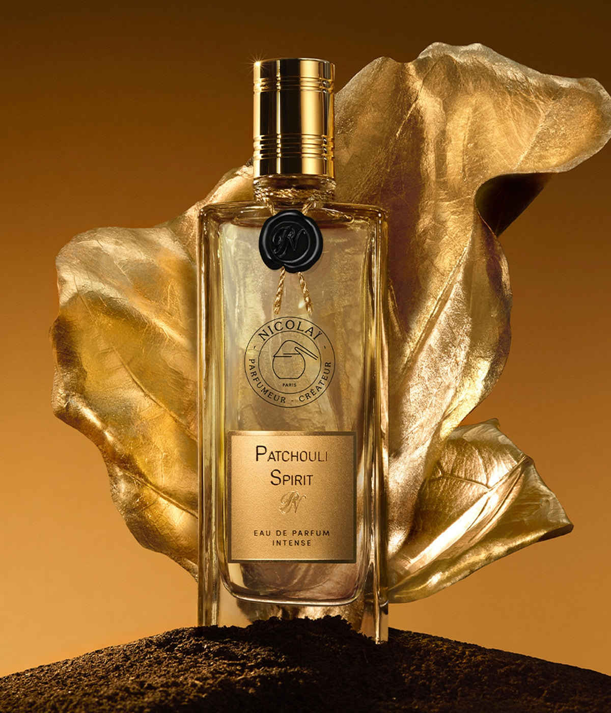 Nicolaï Eau de Parfum Patchouli Spirit vor einem goldenen Blatt auf dunkler Erde