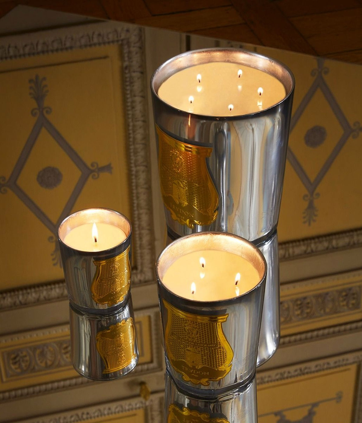 Trudon Cabinet des Miroirs scented candles burning on a mirror against gilded wall paneling