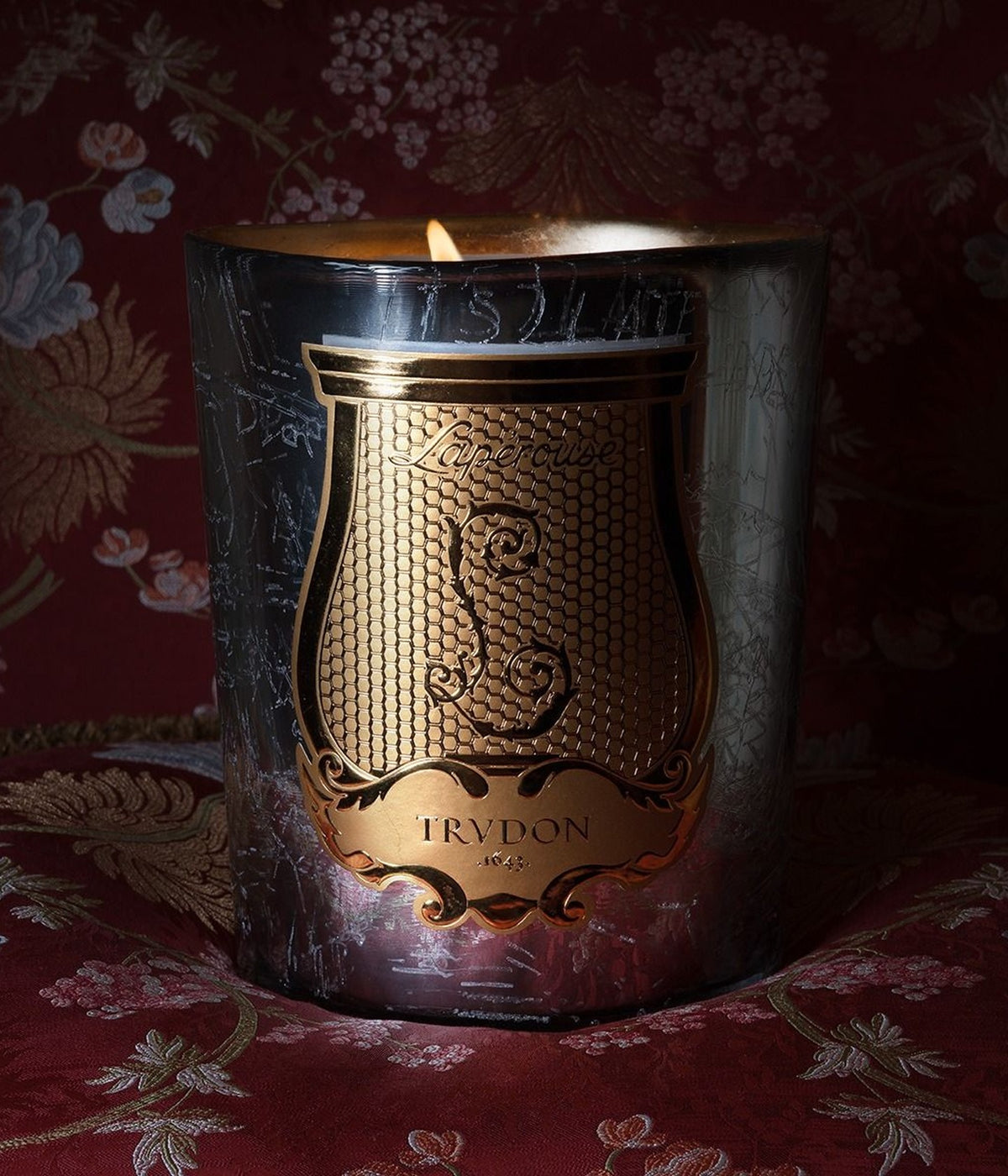Trudon Maison de Plaisirs scented candle burning on red floral damask