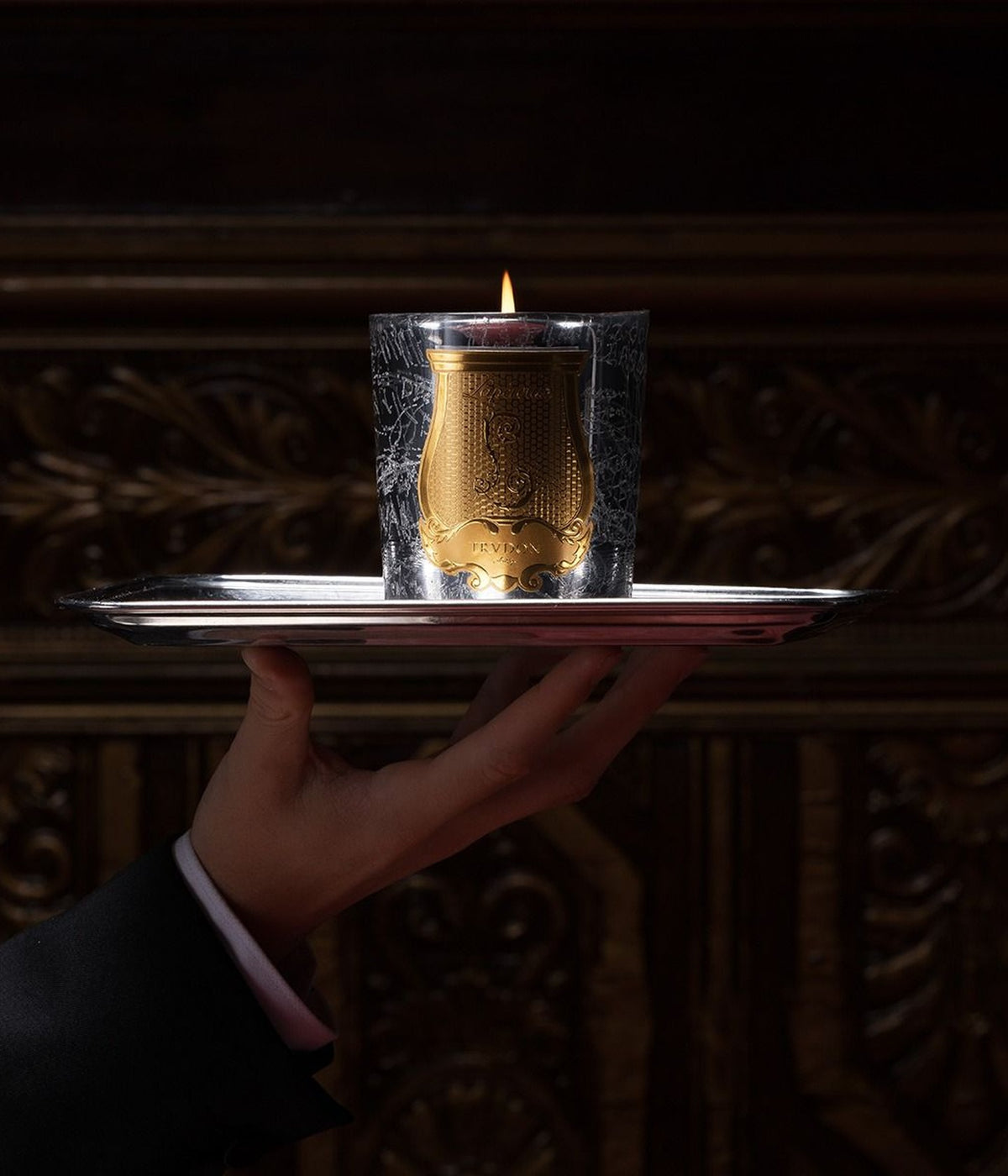 Trudon Maison de Plaisirs scented candle burning on a silver tray held out by a hand