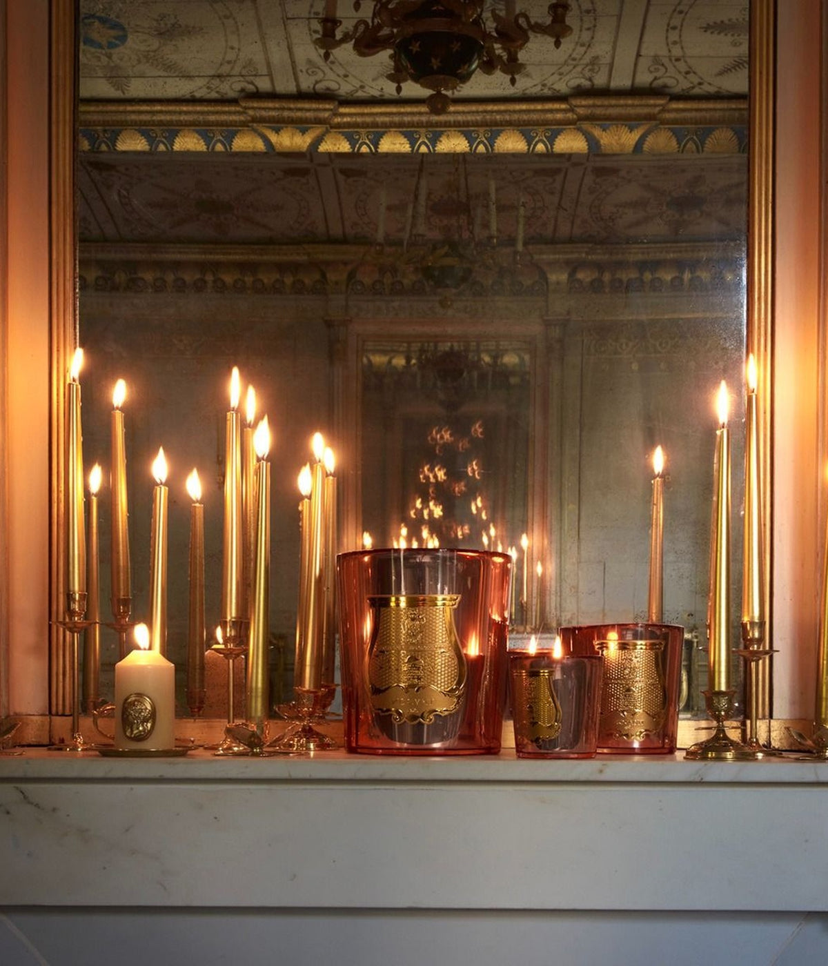 Trudon Nazareth scented candles among lit taper candles on a mantelpiece in front of a mirror